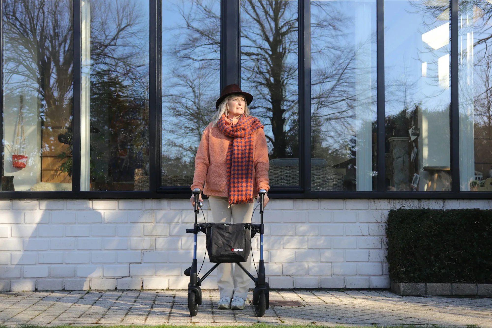 An older woman with a walking frame by a large window
